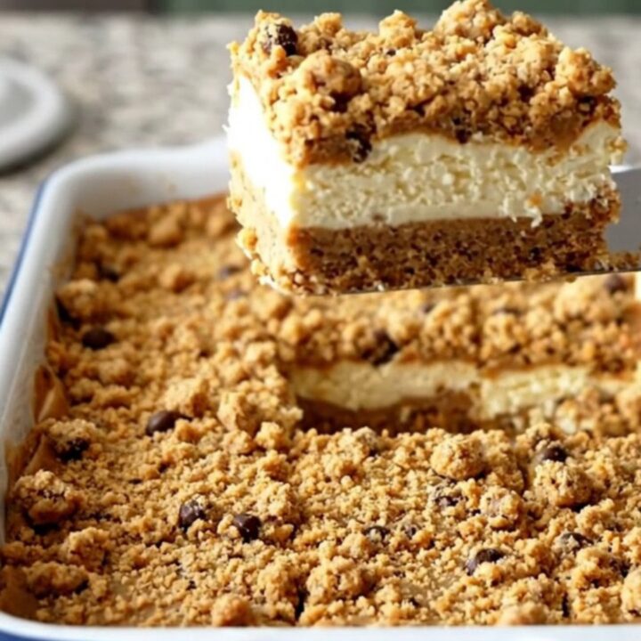 A top-down view of chocolate chip cookie cheesecake bars in a white baker on a speckled granite surface.