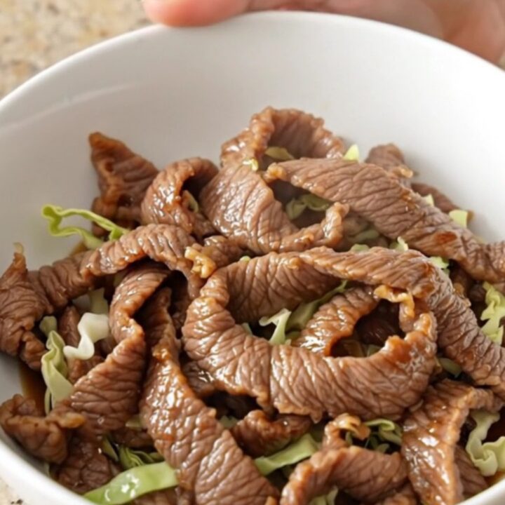 A close-up of a bowl filled with tender steak strips, shredded cabbage, and carrots in a savory soy-ginger sauce.