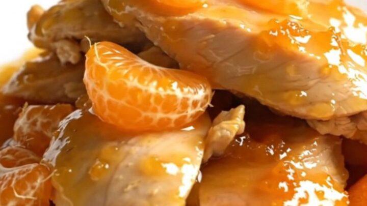 A close-up of slow-cooked chicken tenderloins glazed in a glossy orange sauce with mandarin segments.