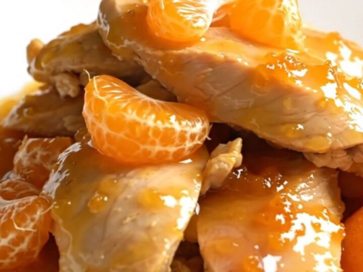 A close-up of slow-cooked chicken tenderloins glazed in a glossy orange sauce with mandarin segments.