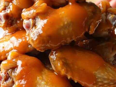 A close-up view of slow-cooked apricot sriracha chicken wings served on a white plate.