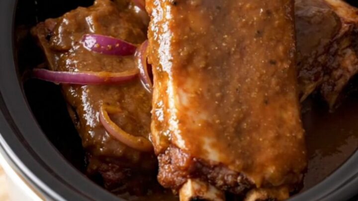A close-up of slow-cooked jerk spareribs served on a wooden board, showing a dark, glossy glaze and tender meat.