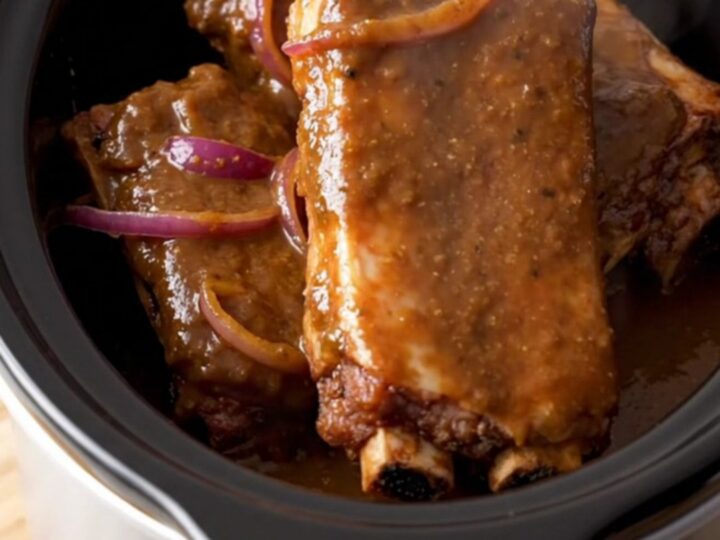 A close-up of slow-cooked jerk spareribs served on a wooden board, showing a dark, glossy glaze and tender meat.
