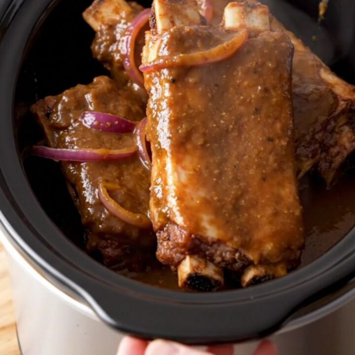 A close-up of slow-cooked jerk spareribs served on a wooden board, showing a dark, glossy glaze and tender meat.