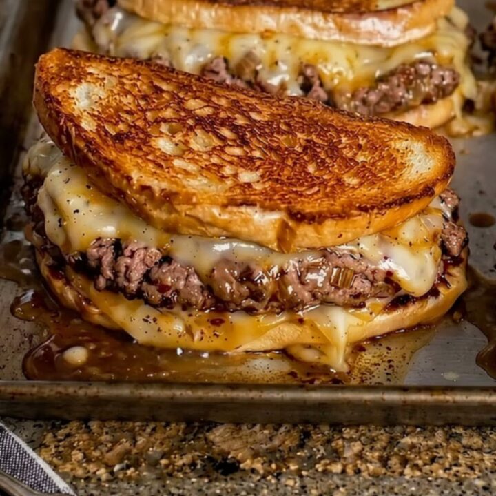 A close-up of a golden-brown patty melt, pulled apart to reveal gooey melted Swiss cheese and seasoned beef.