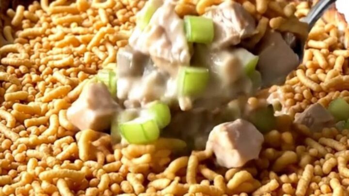 A golden, bubbly chicken casserole topped with crispy chow mein noodles in a white ceramic dish.