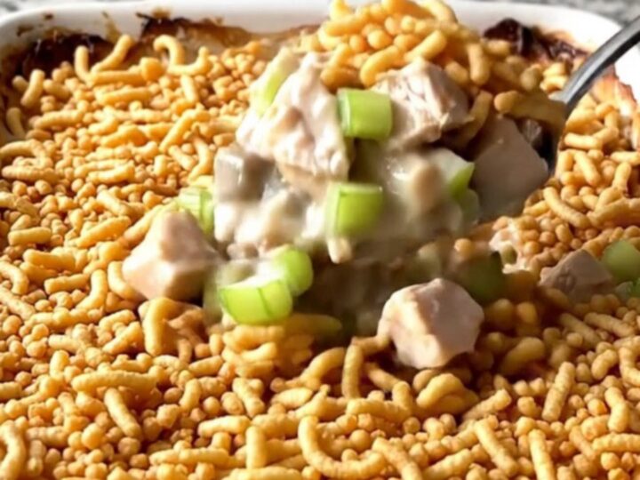 A golden, bubbly chicken casserole topped with crispy chow mein noodles in a white ceramic dish.