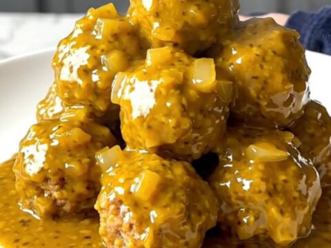 A close-up of tender turkey meatballs coated in a thick, golden mustard barbecue sauce in a slow cooker.