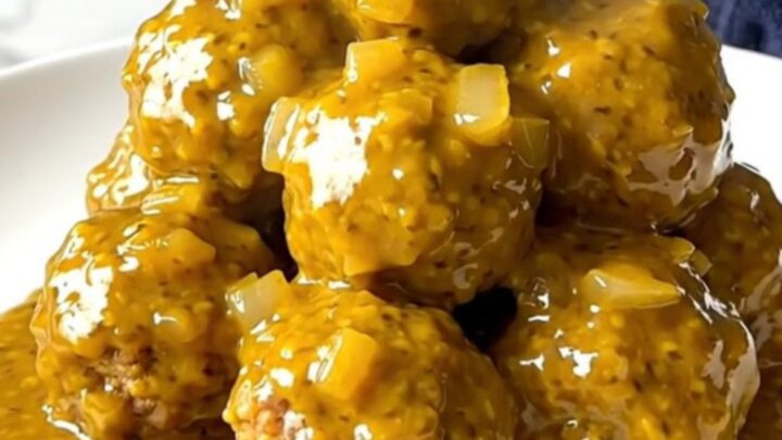 A close-up of tender turkey meatballs coated in a thick, golden mustard barbecue sauce in a slow cooker.