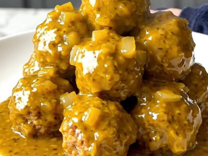 A close-up of tender turkey meatballs coated in a thick, golden mustard barbecue sauce in a slow cooker.
