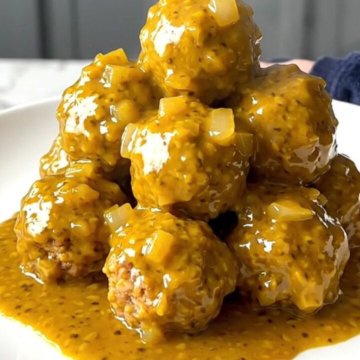 A close-up of tender turkey meatballs coated in a thick, golden mustard barbecue sauce in a slow cooker.
