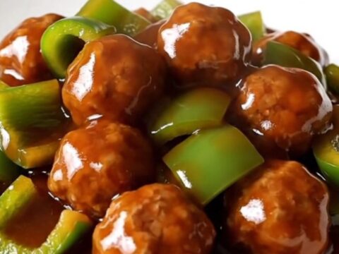 A slow cooker filled with glazed Szechuan meatballs and green bell peppers.