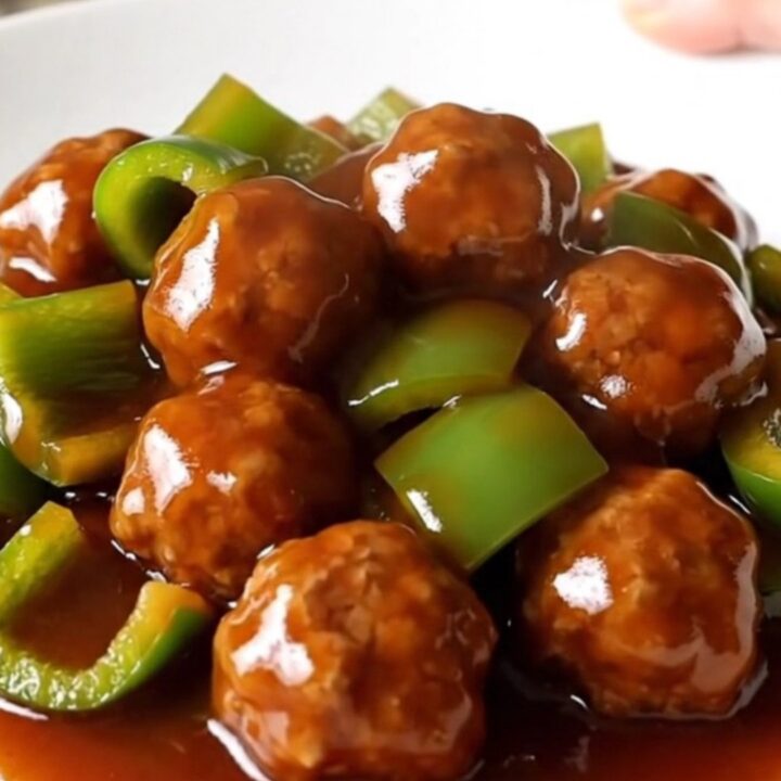 A slow cooker filled with glazed Szechuan meatballs and green bell peppers.