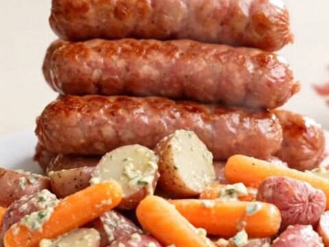 Slow cooker filled with bratwurst links, halved red potatoes, and baby carrots in a creamy ranch broth.