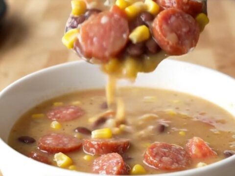 A close-up of a white bowl filled with creamy cowgirl soup featuring smoked sausage coins, corn, and beans.