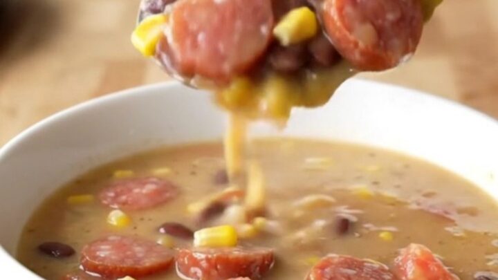 A close-up of a white bowl filled with creamy cowgirl soup featuring smoked sausage coins, corn, and beans.