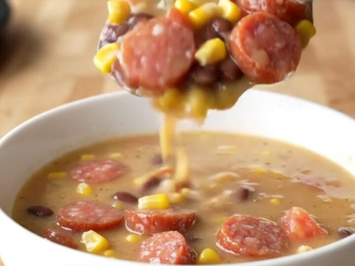 A close-up of a white bowl filled with creamy cowgirl soup featuring smoked sausage coins, corn, and beans.