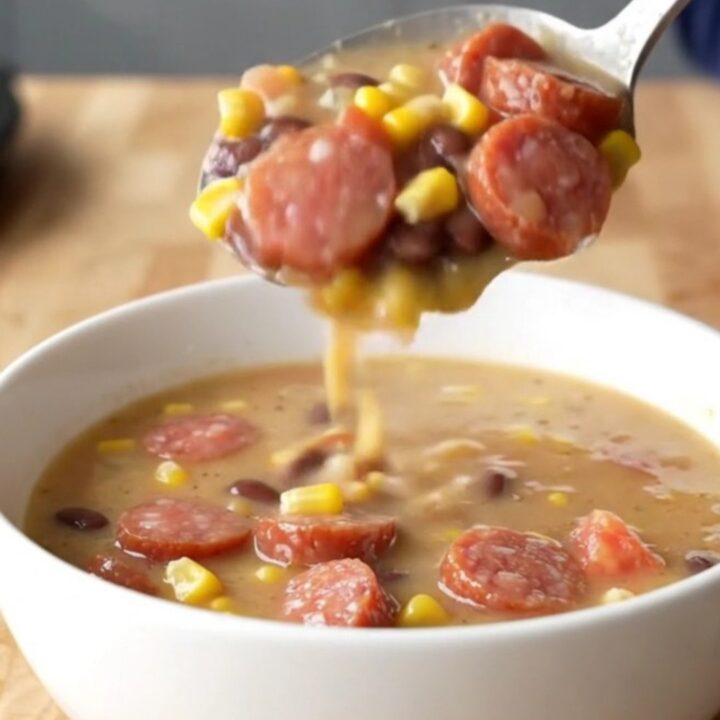 A close-up of a white bowl filled with creamy cowgirl soup featuring smoked sausage coins, corn, and beans.
