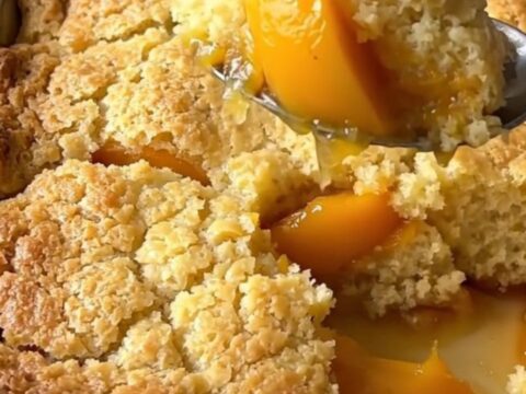 A large rectangular ceramic dish filled with golden-brown baked peach cobbler on a butcher-block counter.