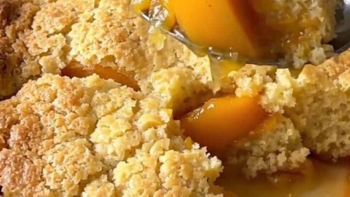 A large rectangular ceramic dish filled with golden-brown baked peach cobbler on a butcher-block counter.