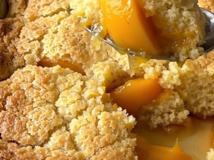 A large rectangular ceramic dish filled with golden-brown baked peach cobbler on a butcher-block counter.