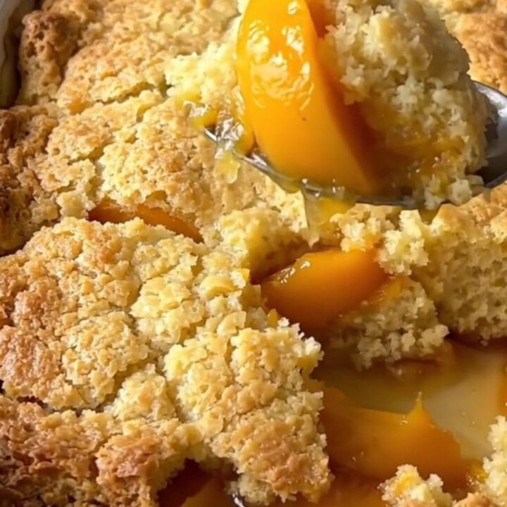 A large rectangular ceramic dish filled with golden-brown baked peach cobbler on a butcher-block counter.