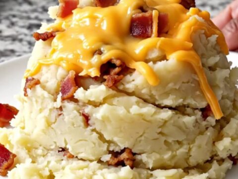 A top-down view of a slow cooker filled with creamy mashed potatoes, bacon, and melted cheddar cheese.