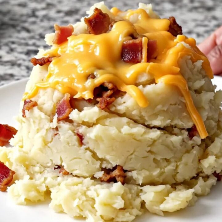 A top-down view of a slow cooker filled with creamy mashed potatoes, bacon, and melted cheddar cheese.