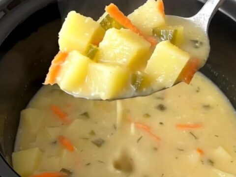 A bowl of creamy dill pickle potato soup with visible chunks of potato, pickle, and carrot garnish.