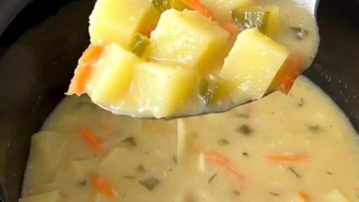 A bowl of creamy dill pickle potato soup with visible chunks of potato, pickle, and carrot garnish.