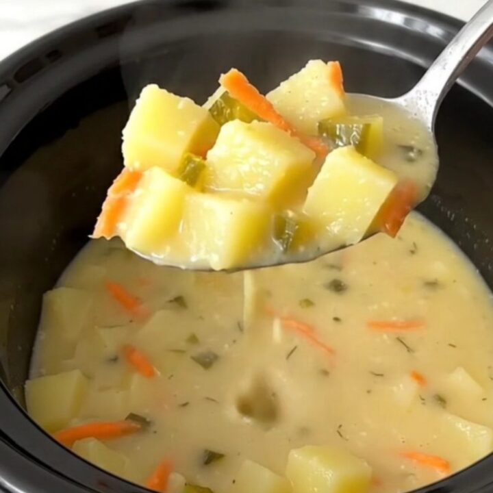 A bowl of creamy dill pickle potato soup with visible chunks of potato, pickle, and carrot garnish.