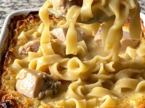 A top-down view of a rectangular baking dish filled with raw chicken, egg noodles, and creamy sauce before baking.