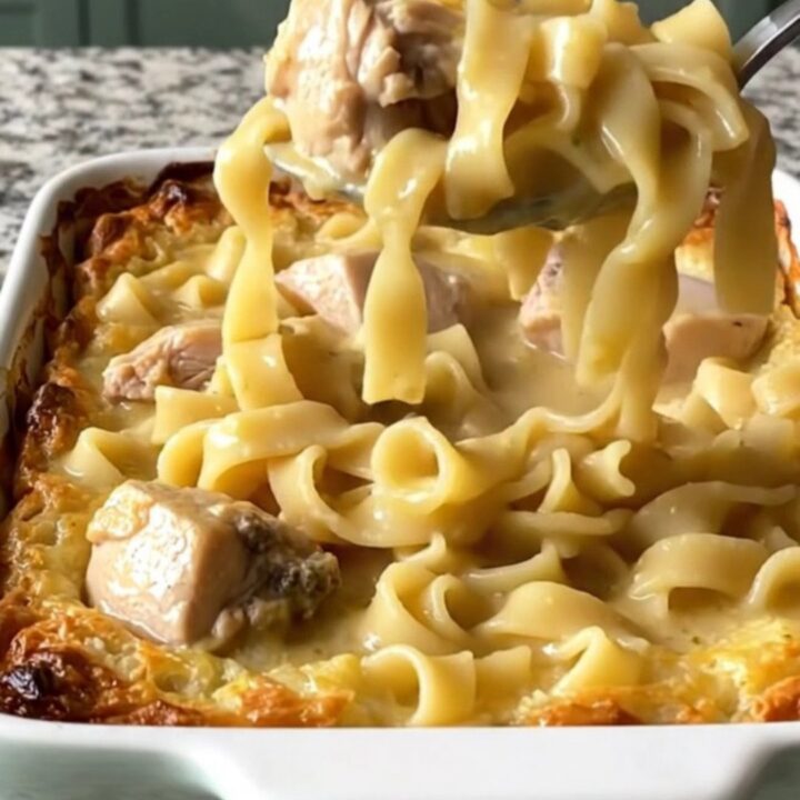 A top-down view of a rectangular baking dish filled with raw chicken, egg noodles, and creamy sauce before baking.