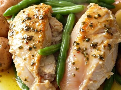 A top-down view of a slow cooker filled with chicken breasts, green beans, and baby potatoes seasoned with Italian herbs.