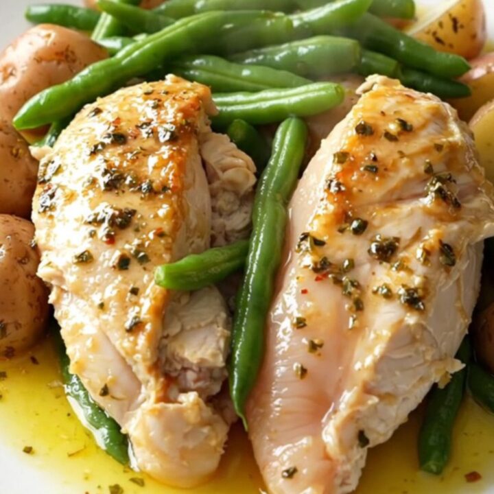 A top-down view of a slow cooker filled with chicken breasts, green beans, and baby potatoes seasoned with Italian herbs.