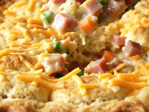 A top-down view of a golden, bubbling ham and cheddar biscuit bake in a white ceramic dish.