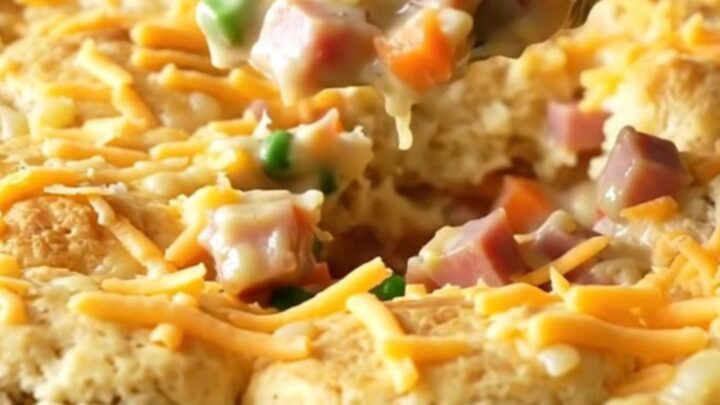 A top-down view of a golden, bubbling ham and cheddar biscuit bake in a white ceramic dish.