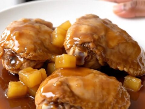A top-down view of raw chicken thighs, pineapple, and brown sugar inside a black slow cooker basin.