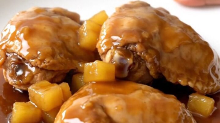A top-down view of raw chicken thighs, pineapple, and brown sugar inside a black slow cooker basin.