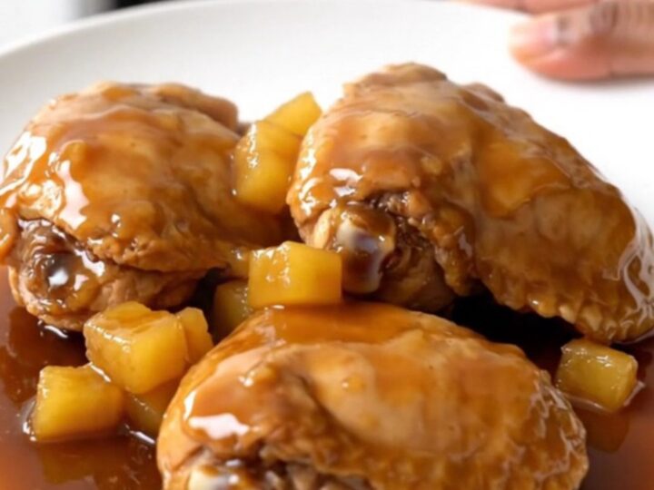 A top-down view of raw chicken thighs, pineapple, and brown sugar inside a black slow cooker basin.