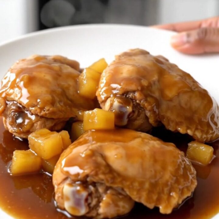 A top-down view of raw chicken thighs, pineapple, and brown sugar inside a black slow cooker basin.