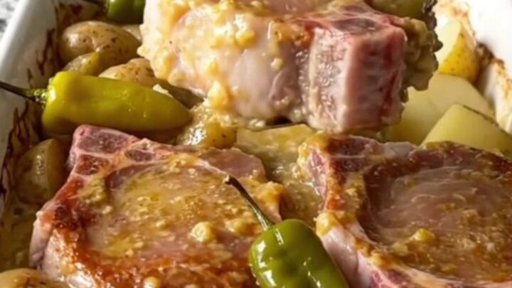 A golden, baked Mississippi pork chop and potato dish in a white ceramic baking dish with pepperoncini peppers.