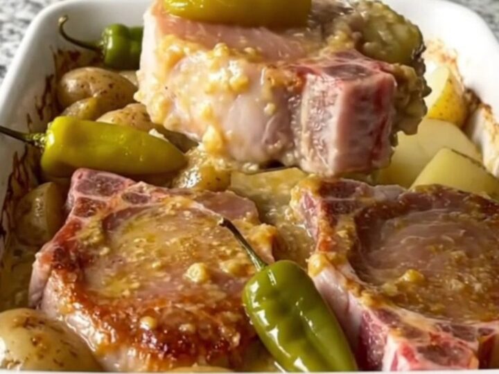 A golden, baked Mississippi pork chop and potato dish in a white ceramic baking dish with pepperoncini peppers.