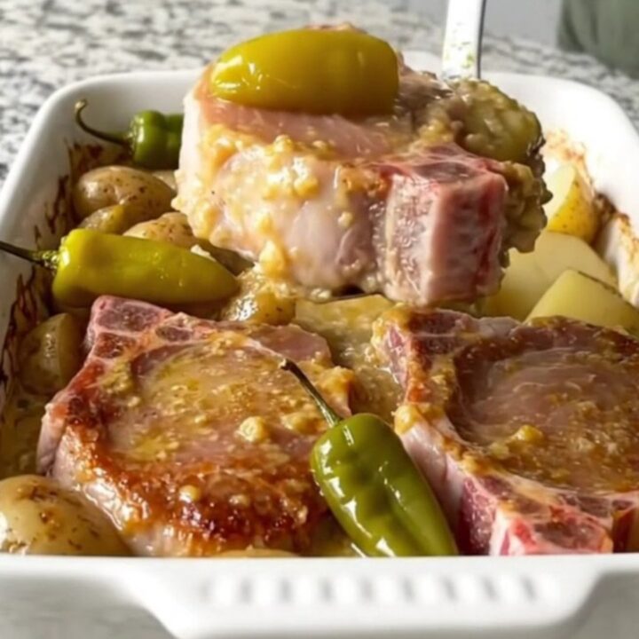 A golden, baked Mississippi pork chop and potato dish in a white ceramic baking dish with pepperoncini peppers.