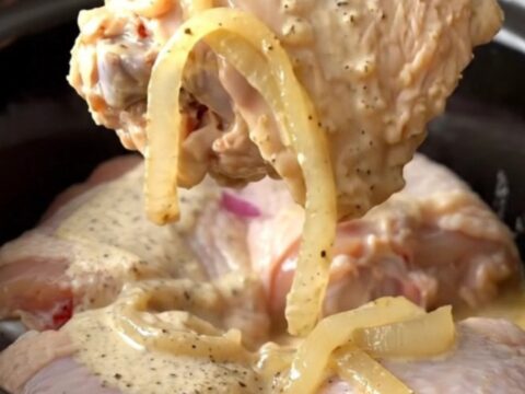 A close-up of tender, braised chicken thighs coated in creamy white barbecue sauce with soft onion slices.