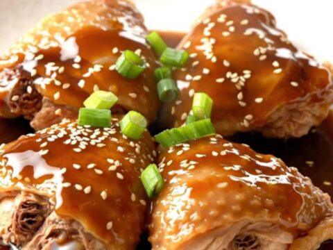 A close-up of tender, braised chicken thighs in a dark, glossy Japanese barbecue sauce