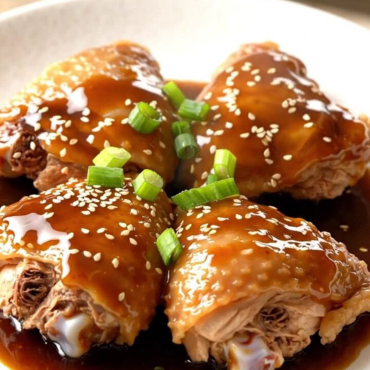 A close-up of tender, braised chicken thighs in a dark, glossy Japanese barbecue sauce
