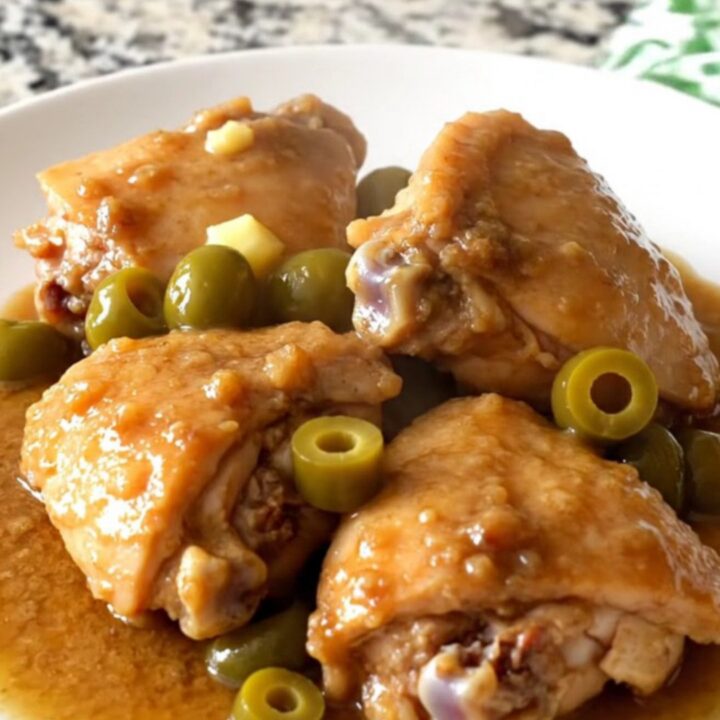 A rustic slow cooker filled with tender chicken thighs, baby red potatoes, and pepperoncini in a rich brown gravy.