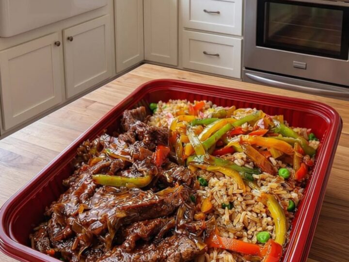 A vibrant serving of pepper steak stir-fry with vegetable fried rice in a red rectangular container.