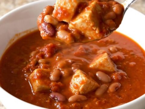 A close-up of a steaming bowl of three bean chicken chili in a white shallow bowl.
